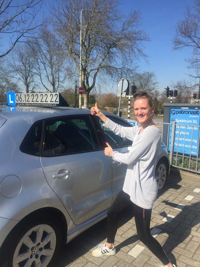 Geslaagde leerling met duimen omhoog naast de lesauto van Rijschool Amsterdam