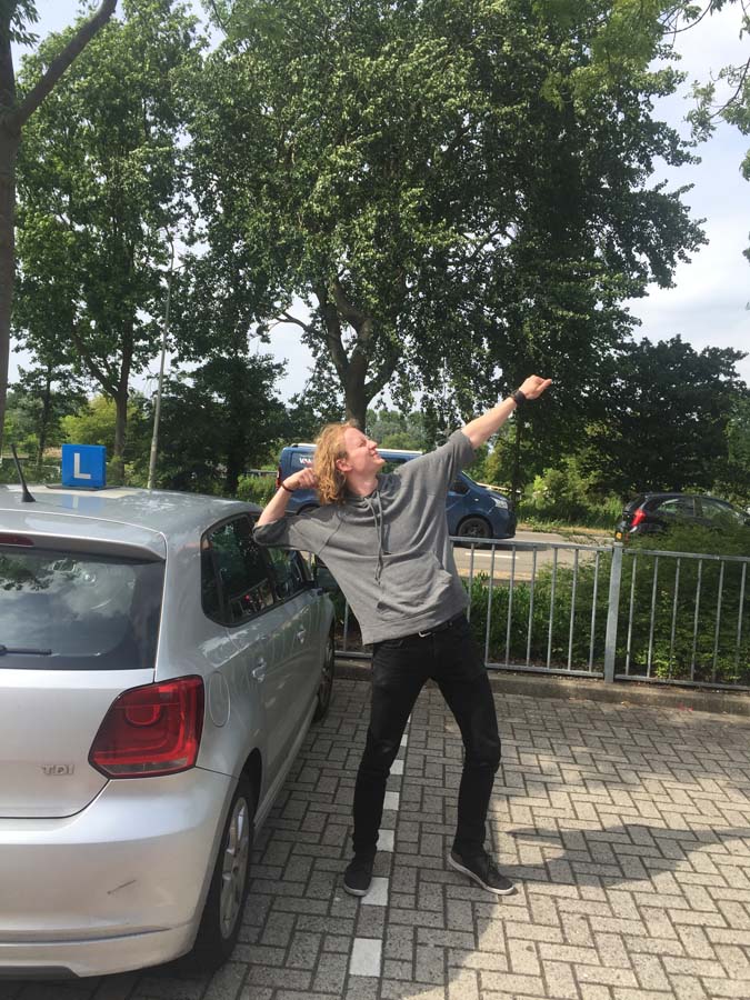 Geslaagde leerling met duimen omhoog naast de lesauto van Rijschool Amsterdam