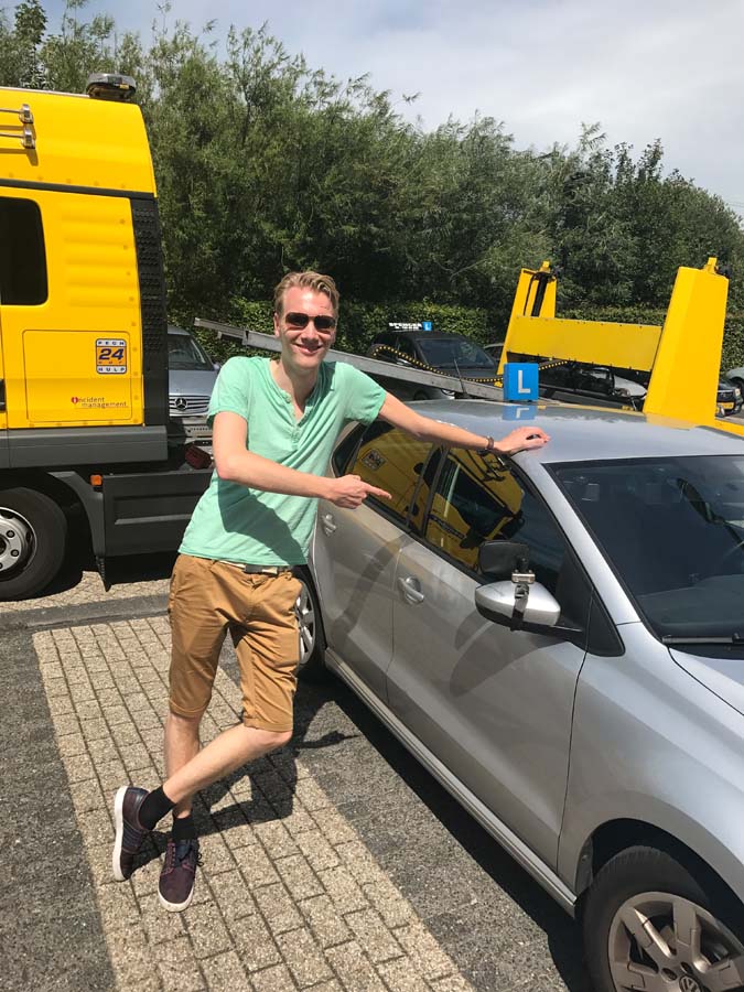Geslaagde leerling met duimen omhoog naast de lesauto van Rijschool Amsterdam