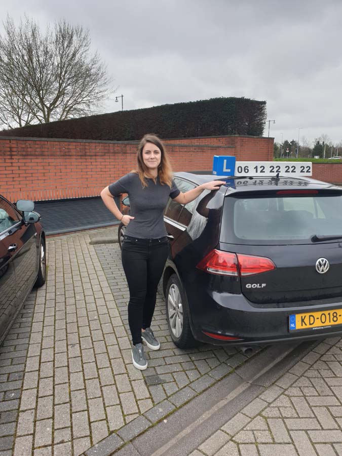 Geslaagde leerling met duimen omhoog naast de lesauto van Rijschool Amsterdam